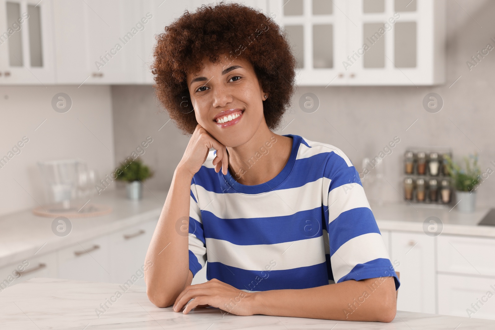 Photo of Happy young woman sitting at table in kitchen