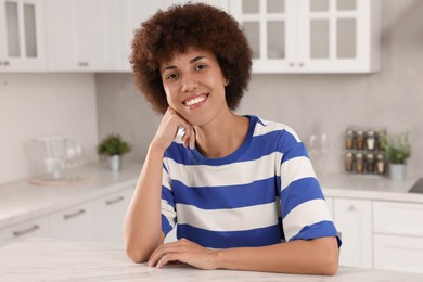 Happy young woman sitting at table in kitchen