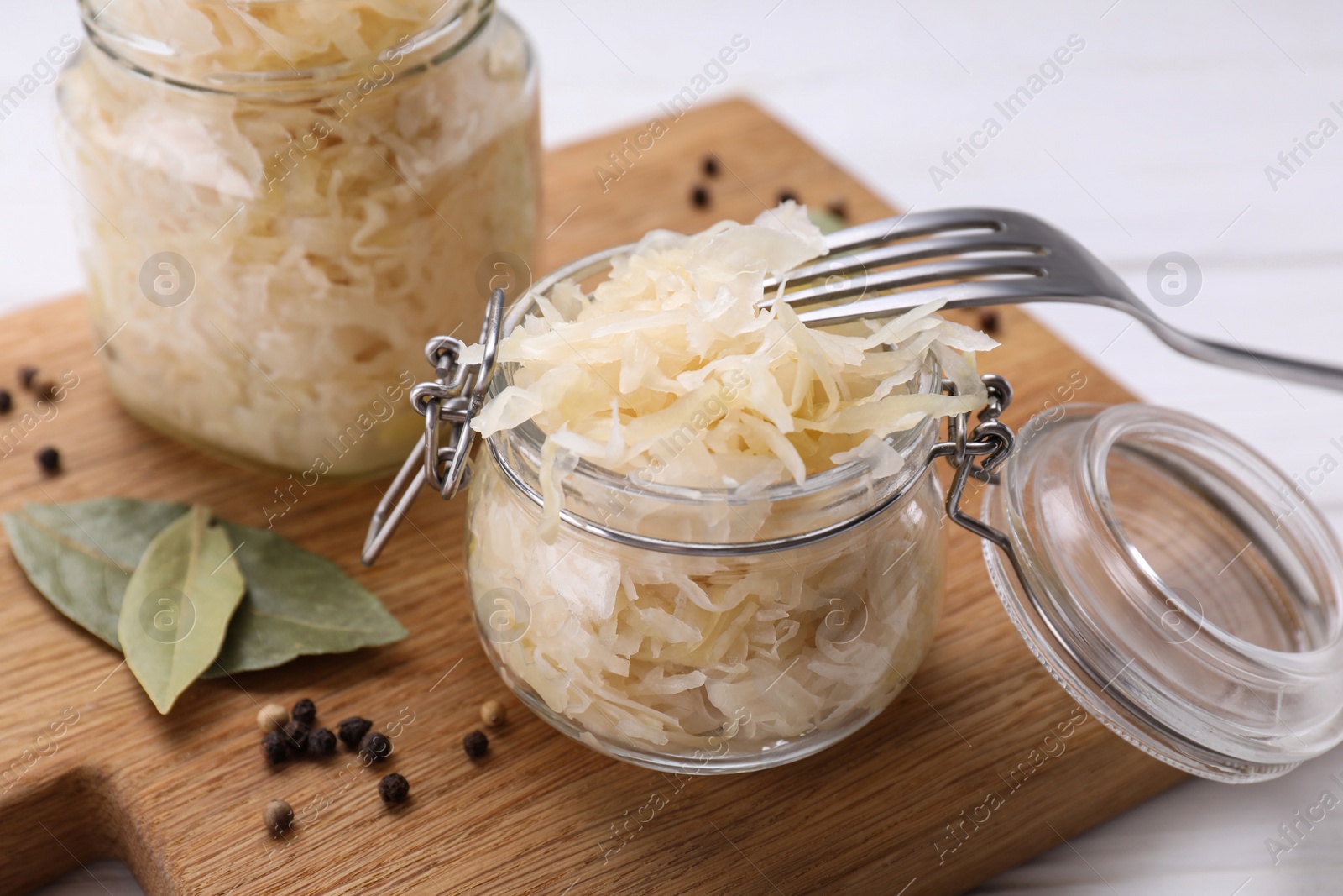 Photo of Glass jars with tasty sauerkraut on white wooden table, closeup