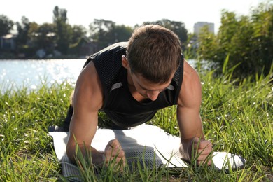 Sporty man doing plank exercise on green grass near river
