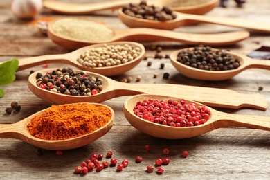 Spoons with different types of pepper on wooden table