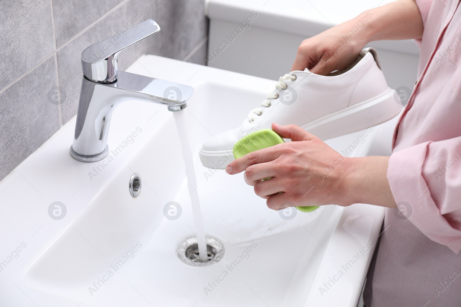 Photo of Woman washing stylish sneakers with brush in sink, closeup