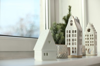 Beautiful house shaped candle holders and small fir trees on windowsill indoors, space for text
