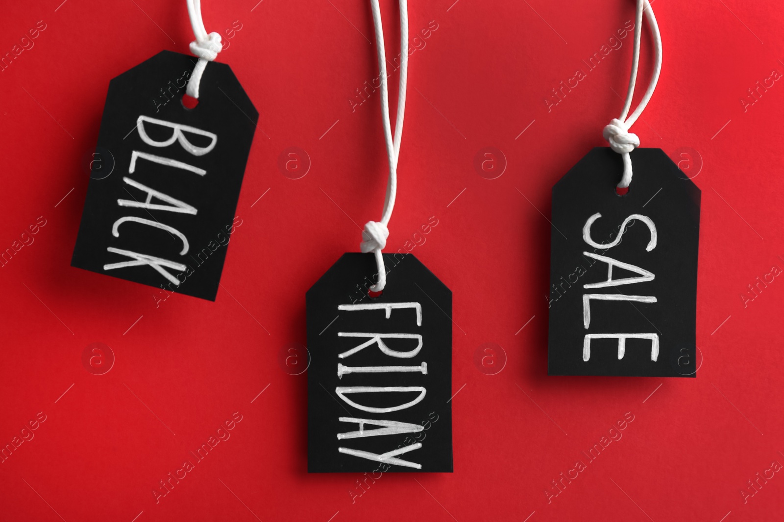 Photo of Tags with words BLACK FRIDAY SALE hanging on red background
