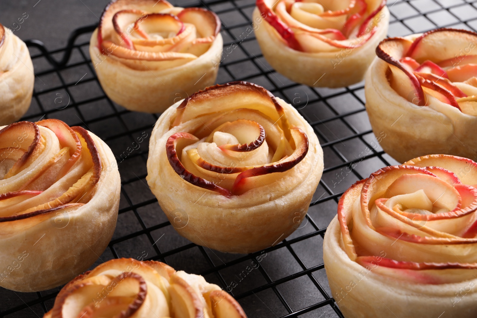 Photo of Cooling rack with freshly baked apple roses on grey table, closeup. Beautiful dessert