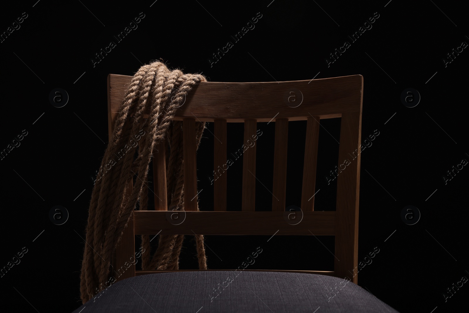 Photo of Hostage concept. Wooden chair and rope on dark background