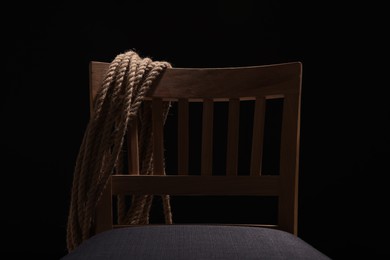 Photo of Hostage concept. Wooden chair and rope on dark background