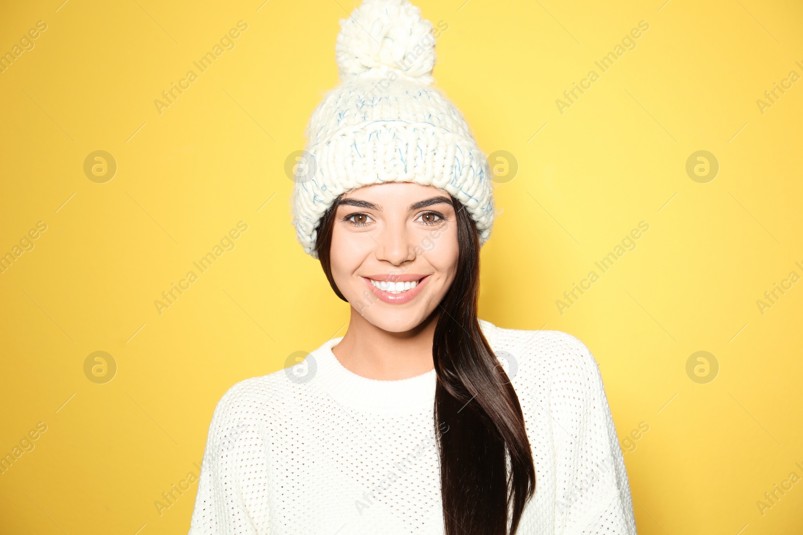 Image of Happy young woman wearing warm sweater and knitted hat on yellow background