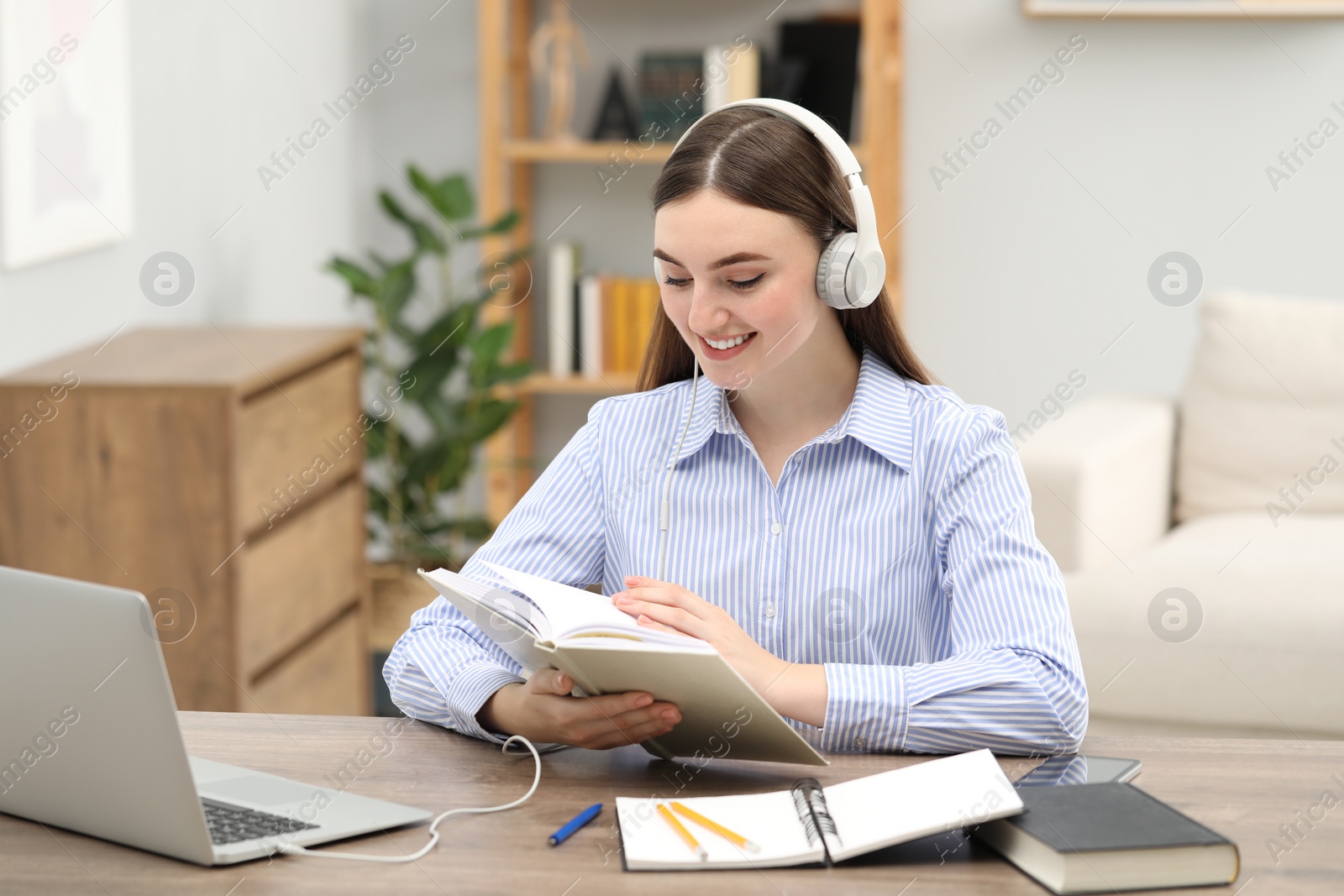 Photo of E-learning. Young woman with book during online lesson at table indoors