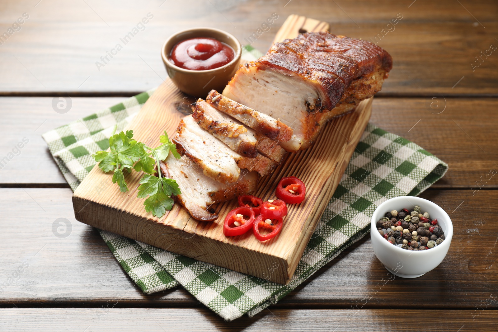 Photo of Pieces of baked pork belly served with sauce, chili pepper and parsley on wooden table