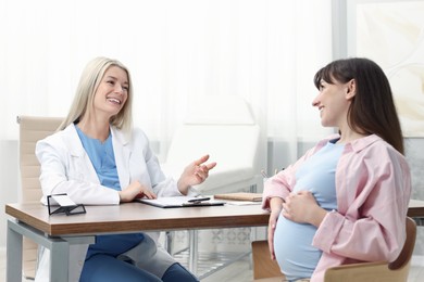 Photo of Smiling doctor consulting pregnant patient at table in clinic