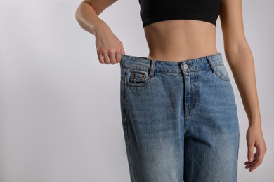 Photo of Skinny woman in oversized jeans on light background, closeup with space for text. Weight loss concept