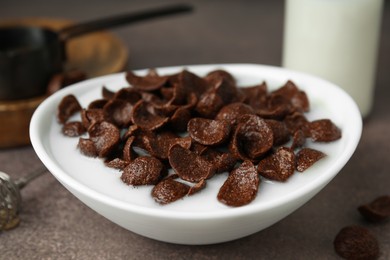 Photo of Breakfast cereal. Chocolate corn flakes and milk in bowl on brown table, closeup