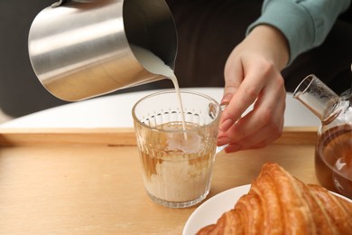 Photo of Woman pouring milk into cup with aromatic tea at table indoors, closeup