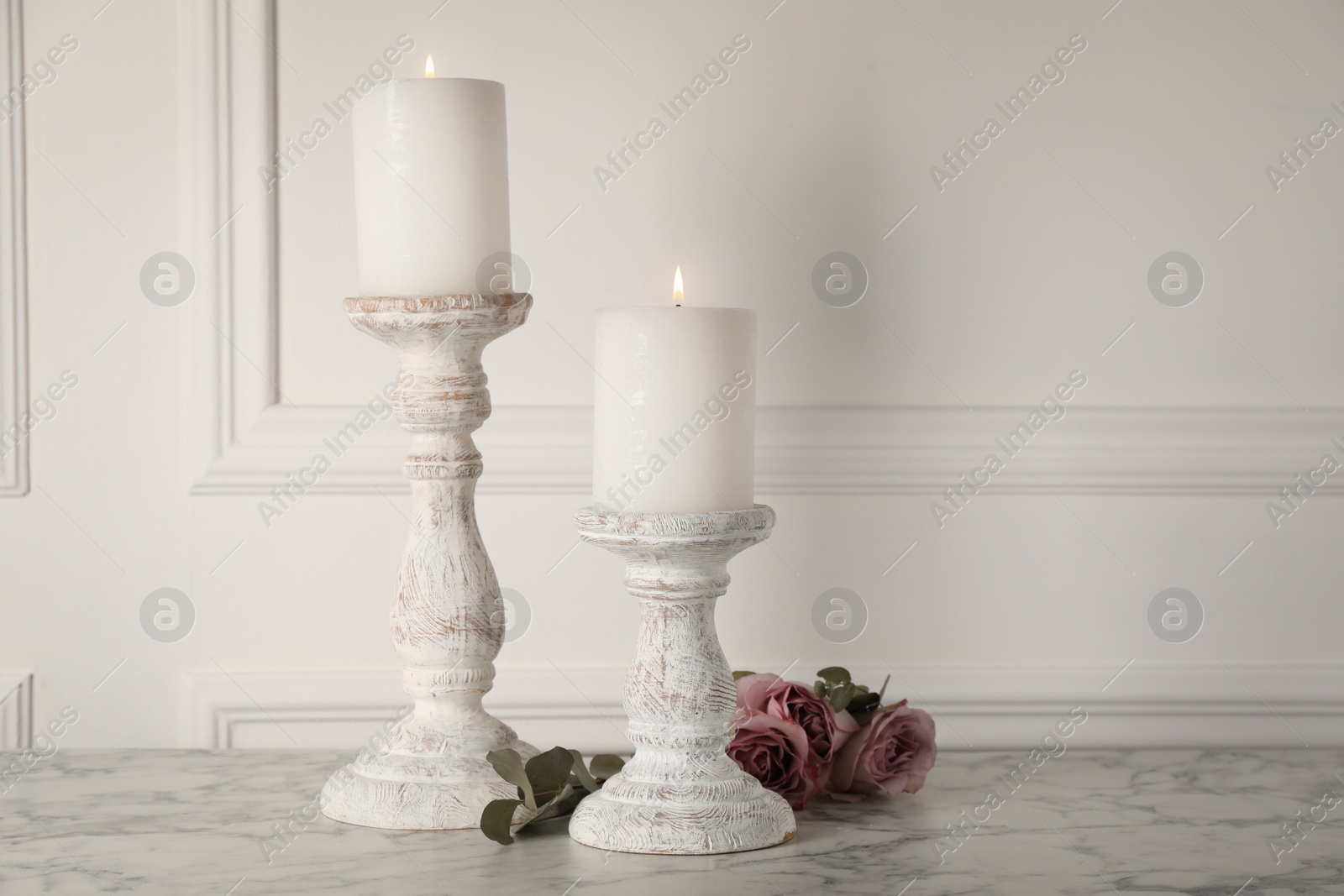 Photo of Elegant candlesticks with burning candles and flowers on white marble table