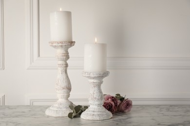 Photo of Elegant candlesticks with burning candles and flowers on white marble table