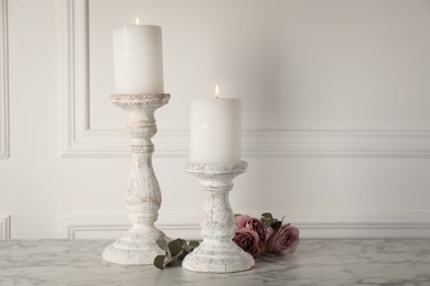 Elegant candlesticks with burning candles and flowers on white marble table