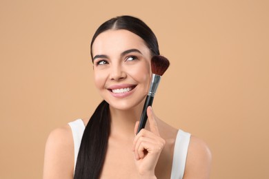 Photo of Beautiful woman with makeup brush on light brown background