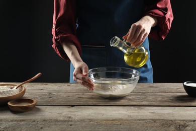 Photo of Making bread. Woman pouring oil into bowl at wooden table, closeup