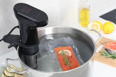 Photo of Sous vide cooker and vacuum packed salmon in pot on table, closeup. Thermal immersion circulator