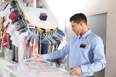 Employee with clothes near counter at dry-cleaner's