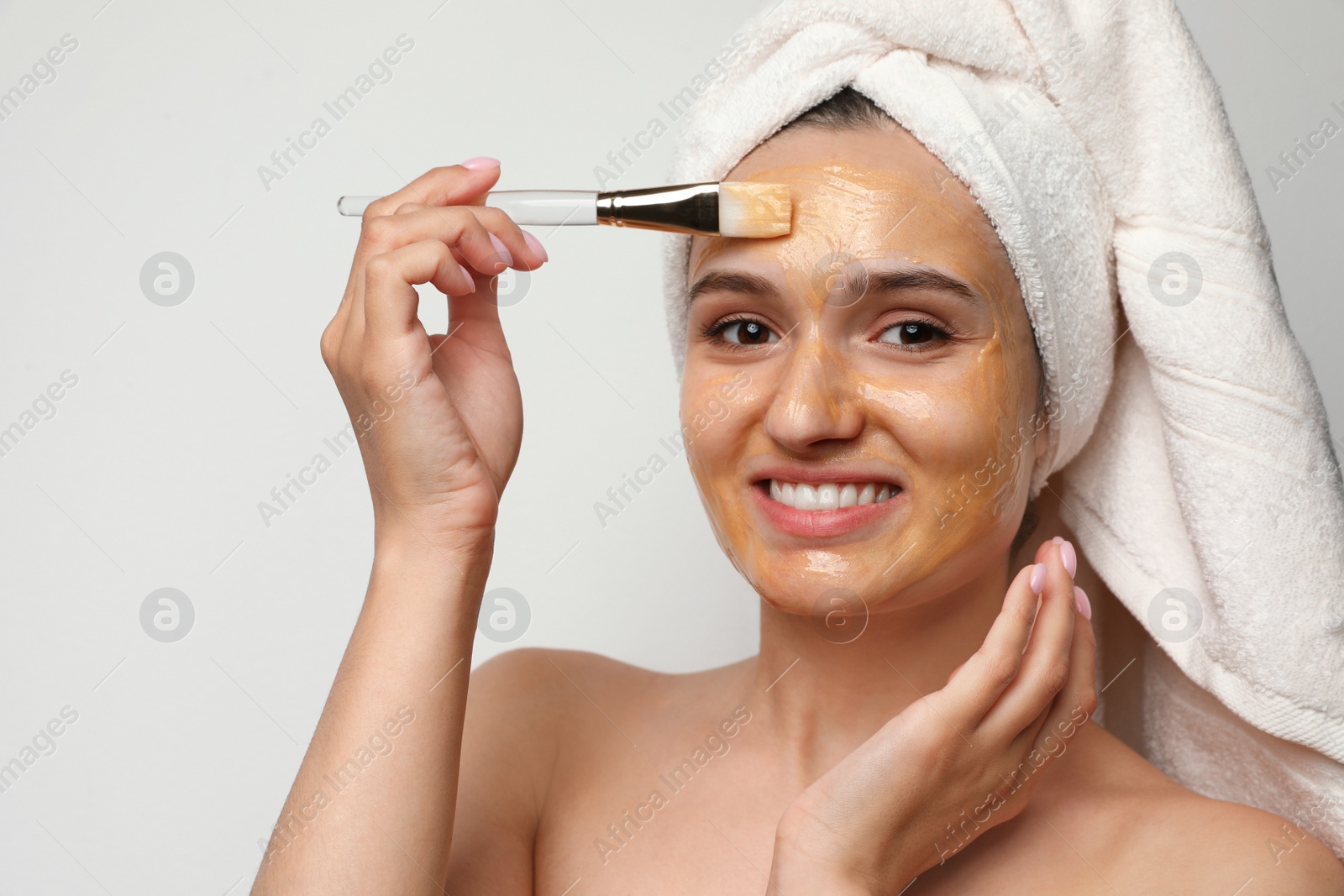 Photo of Beautiful woman applying mask onto face against light background