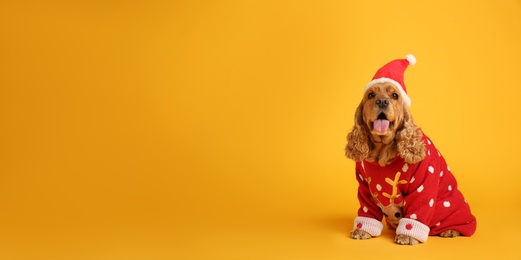 Photo of Adorable Cocker Spaniel in Christmas sweater and Santa hat on yellow background, space for text