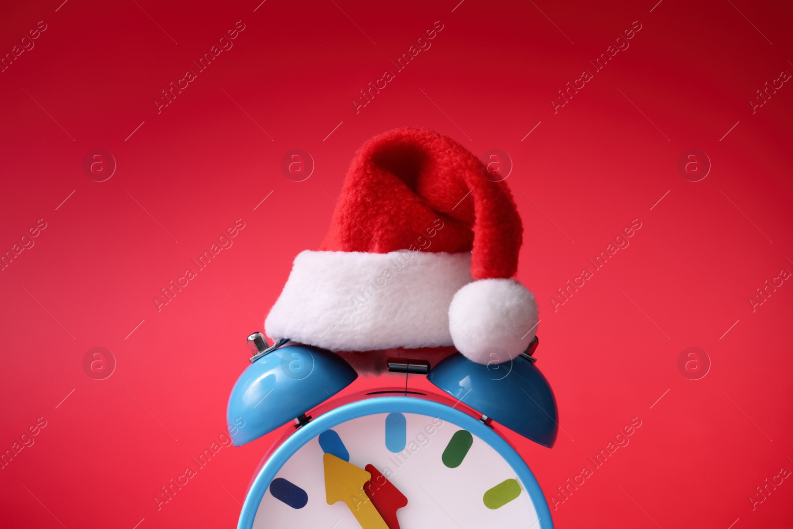 Photo of Alarm clock with Santa hat on red background, closeup. New Year countdown