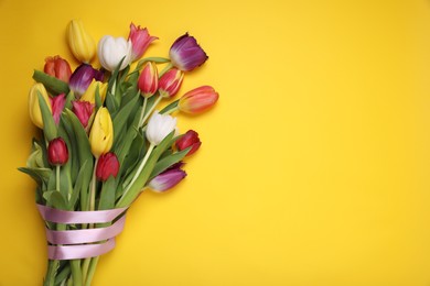 Photo of Bouquet of beautiful colorful tulip flowers tied with pink ribbon on yellow background, top view. Space for text
