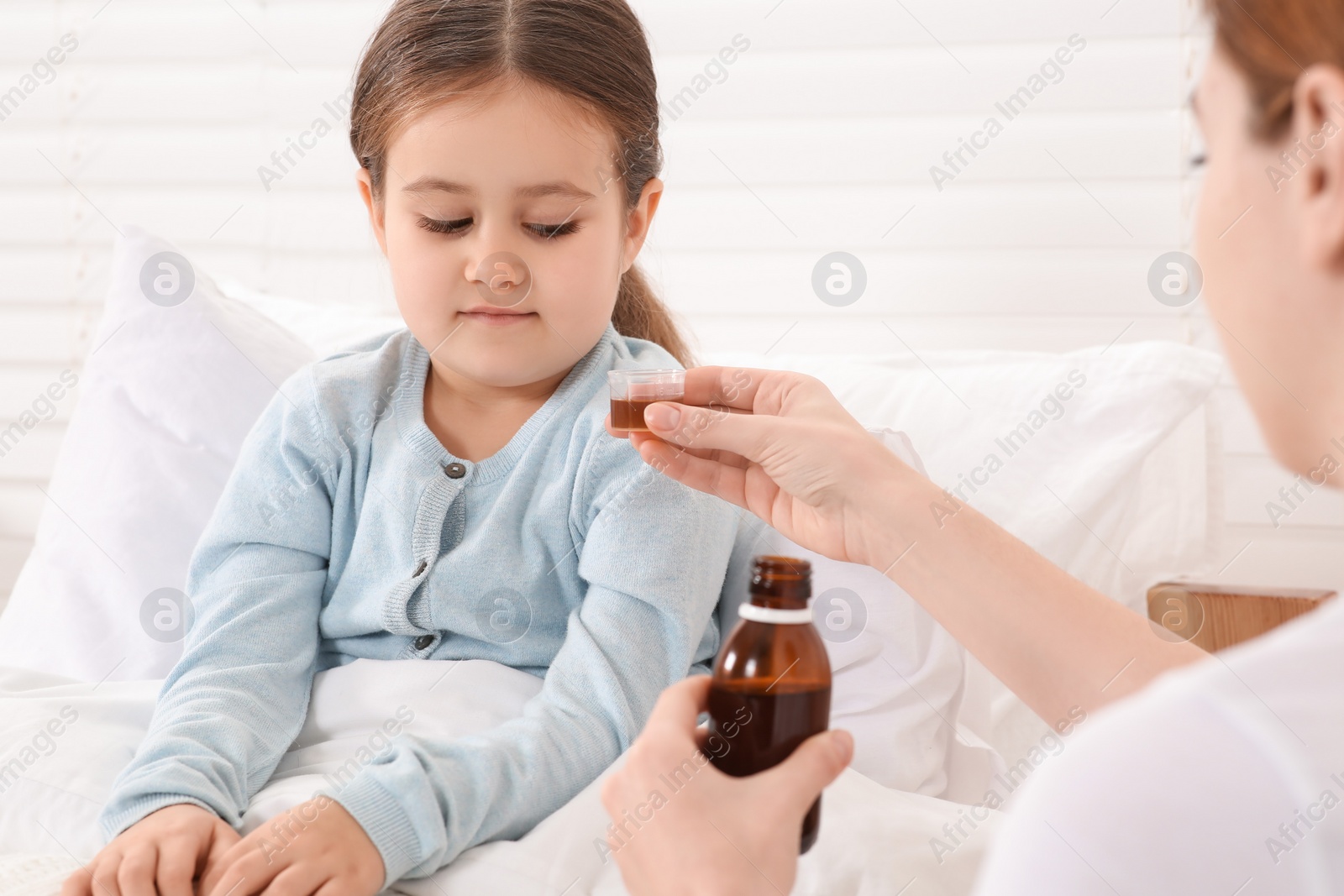 Photo of Mother giving cough syrup to her daughter in bedroom