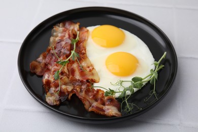 Photo of Fried eggs, bacon and microgreens on white tiled table