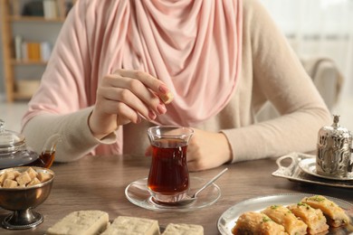 Photo of Woman with cup of delicious Turkish tea at wooden table, closeup