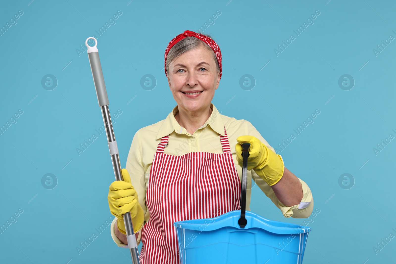 Photo of Happy housewife with mop and bucket on light blue background