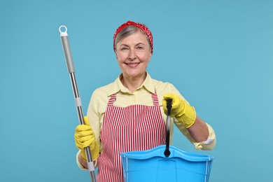 Photo of Happy housewife with mop and bucket on light blue background