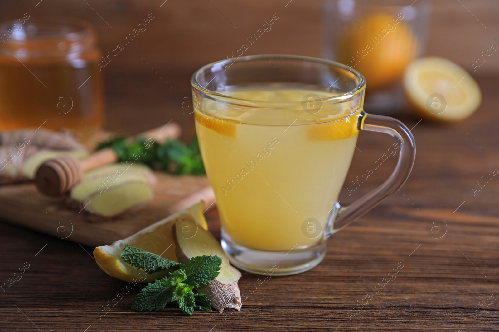 Photo of Glass of aromatic ginger tea and ingredients on wooden table, closeup