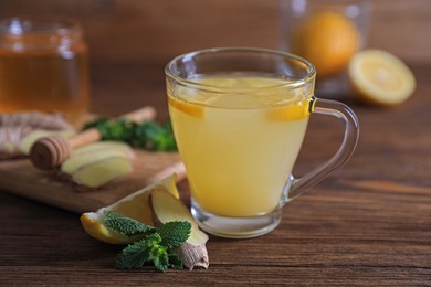 Photo of Glass of aromatic ginger tea and ingredients on wooden table, closeup