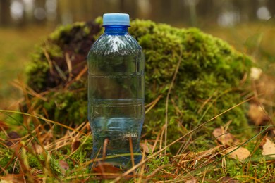 Plastic bottle of fresh water on ground in forest