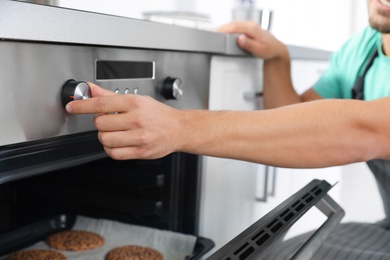 Photo of Young man baking cookies in oven at home, closeup