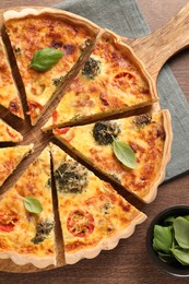 Delicious homemade vegetable quiche and basil leaves on wooden table, flat lay