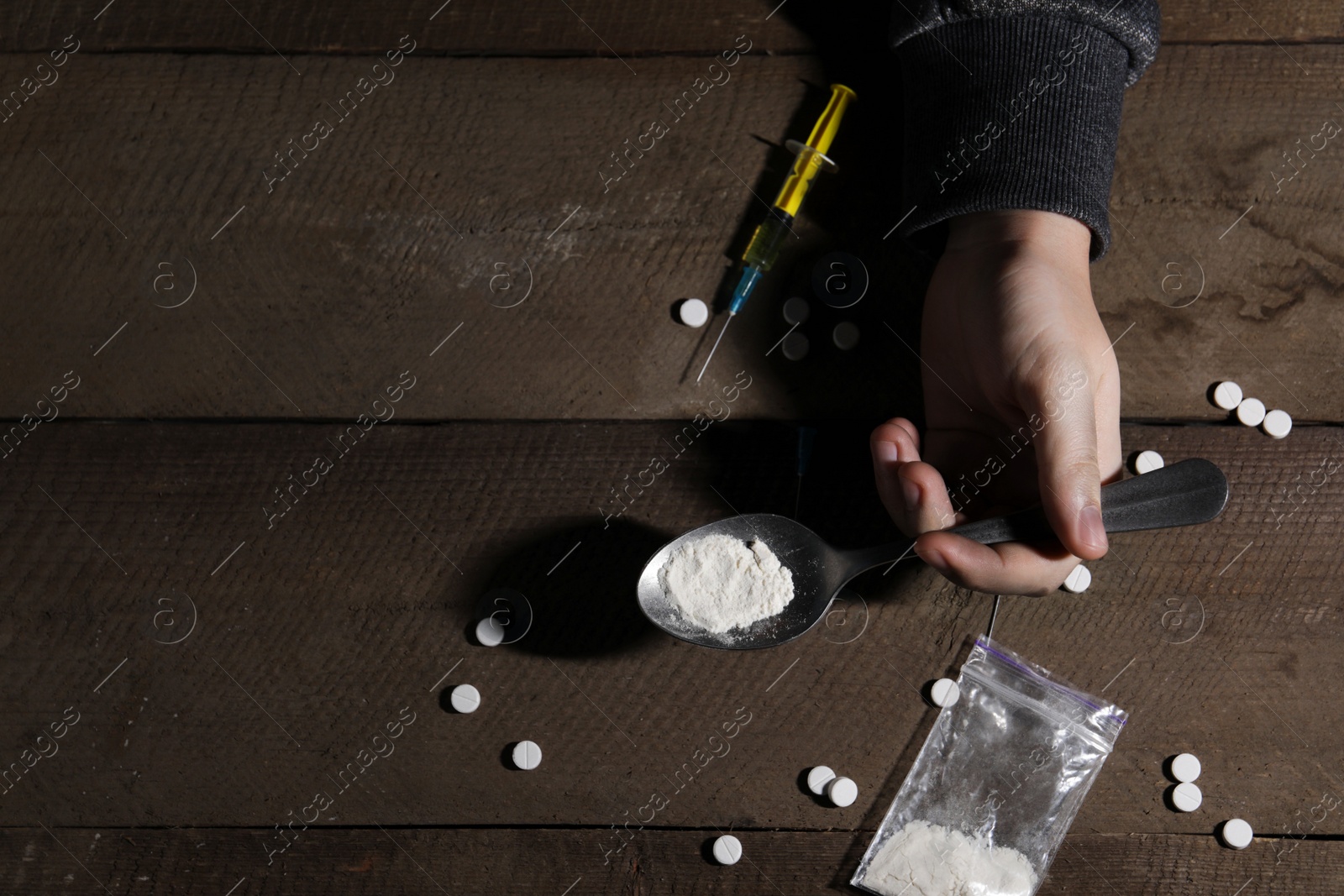 Photo of Addicted man holding spoon with drugs at wooden table, top view. Space for text