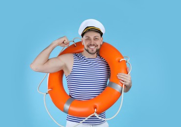 Photo of Sailor with orange ring buoy showing biceps on light blue background