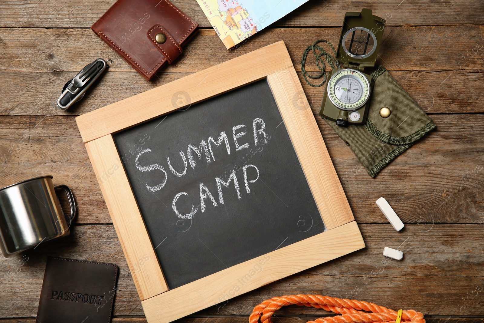 Photo of Chalkboard with text SUMMER CAMP and camping equipment on wooden background, flat lay