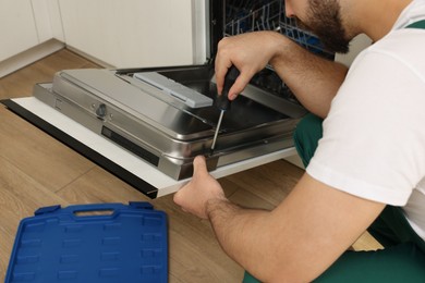 Serviceman repairing dishwasher door with screwdriver indoors, closeup