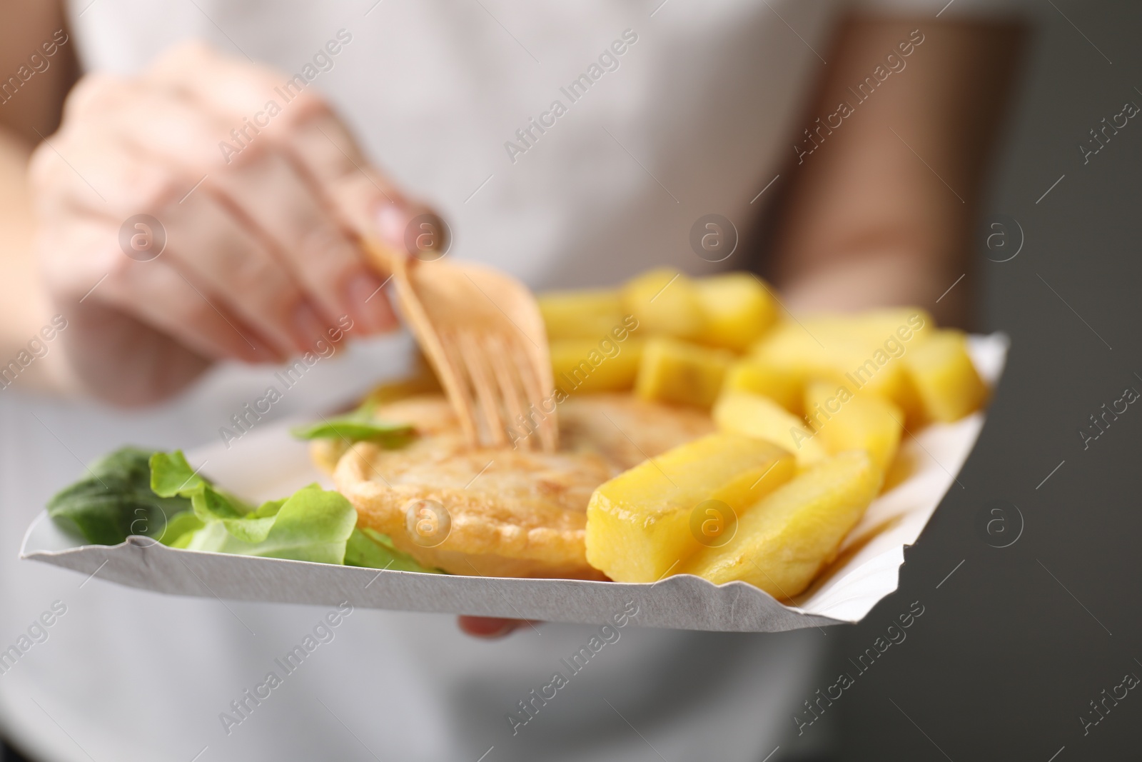 Photo of Woman eating delicious fish and chips on gray background, closeup