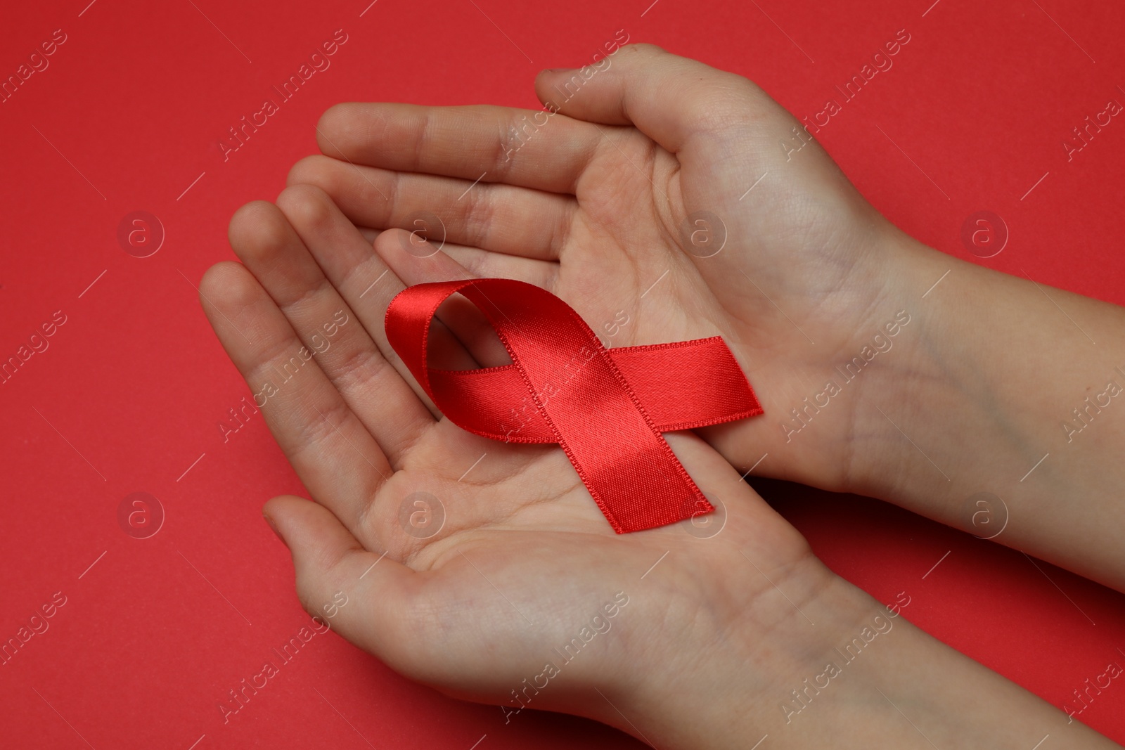 Photo of Little girl holding red ribbon on bright background, closeup. AIDS disease awareness