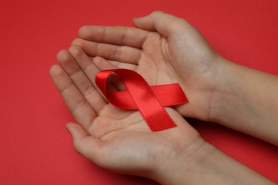 Photo of Little girl holding red ribbon on bright background, closeup. AIDS disease awareness