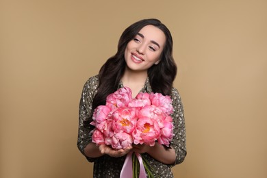 Photo of Beautiful young woman with bouquet of pink peonies on light brown background