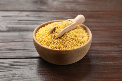 Millet groats in bowl and scoop on wooden table