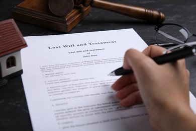 Photo of Woman signing last will and testament at black table, closeup
