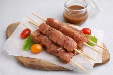 Photo of Wooden skewers with cut raw marinated meat on light grey table